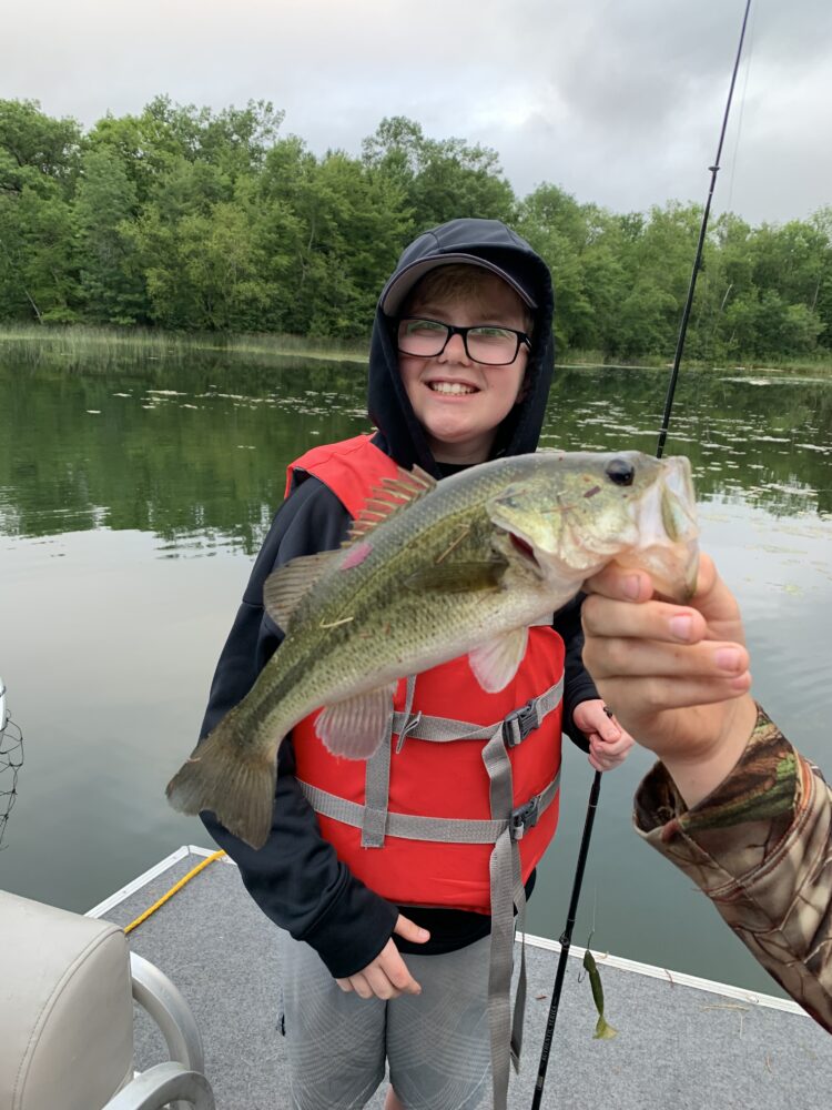 Photo of child holding a fishing pole while someone else's hand is holding up a fish in front of them