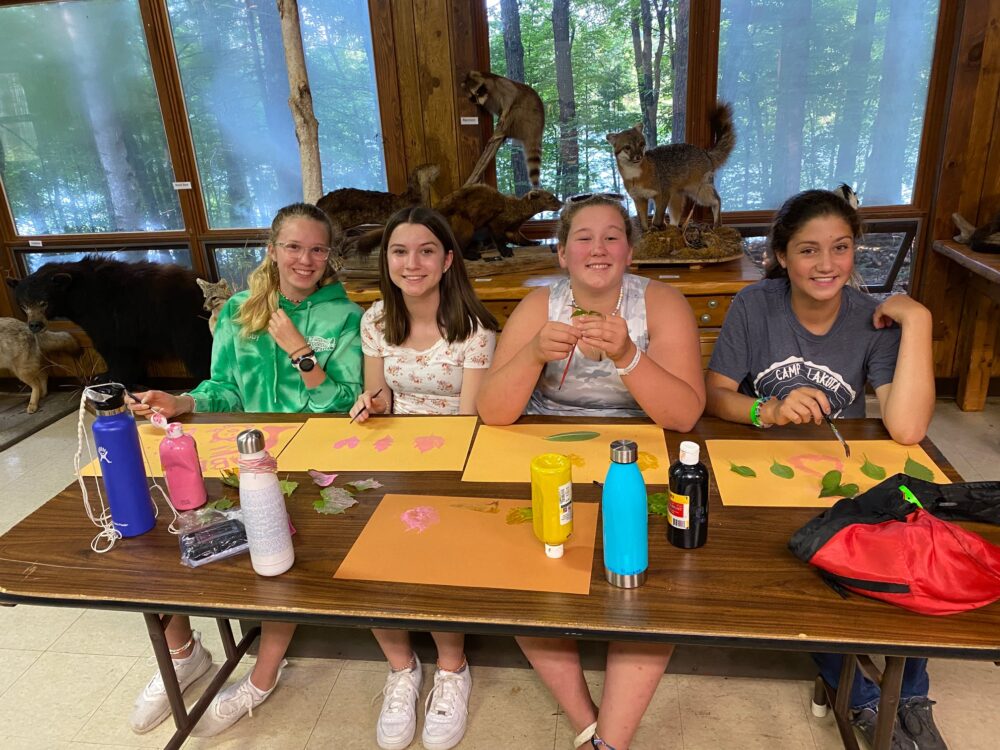 Photo of campers smiling while working on leaf painting in nature center