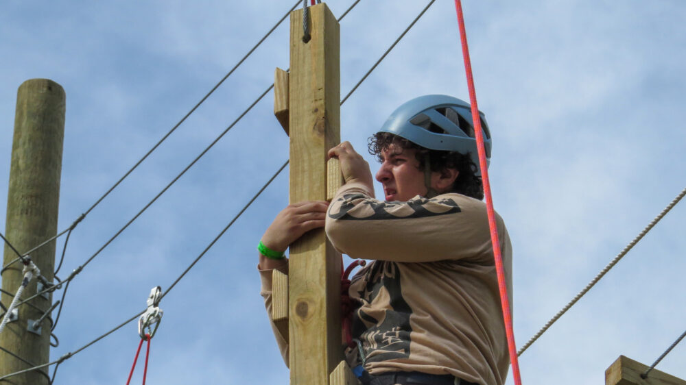 Photo of a person climbing the vertical playpen element of the sun high ropes