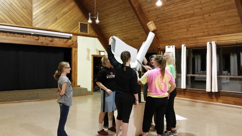 Photo of a group team building activity where people are huddled together and holding paper